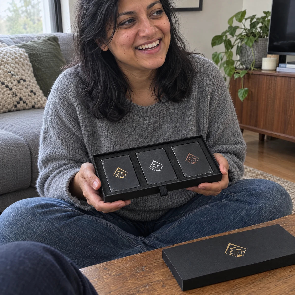 Woman sitting cross-legged with the open Twosome Cards box and three decks.