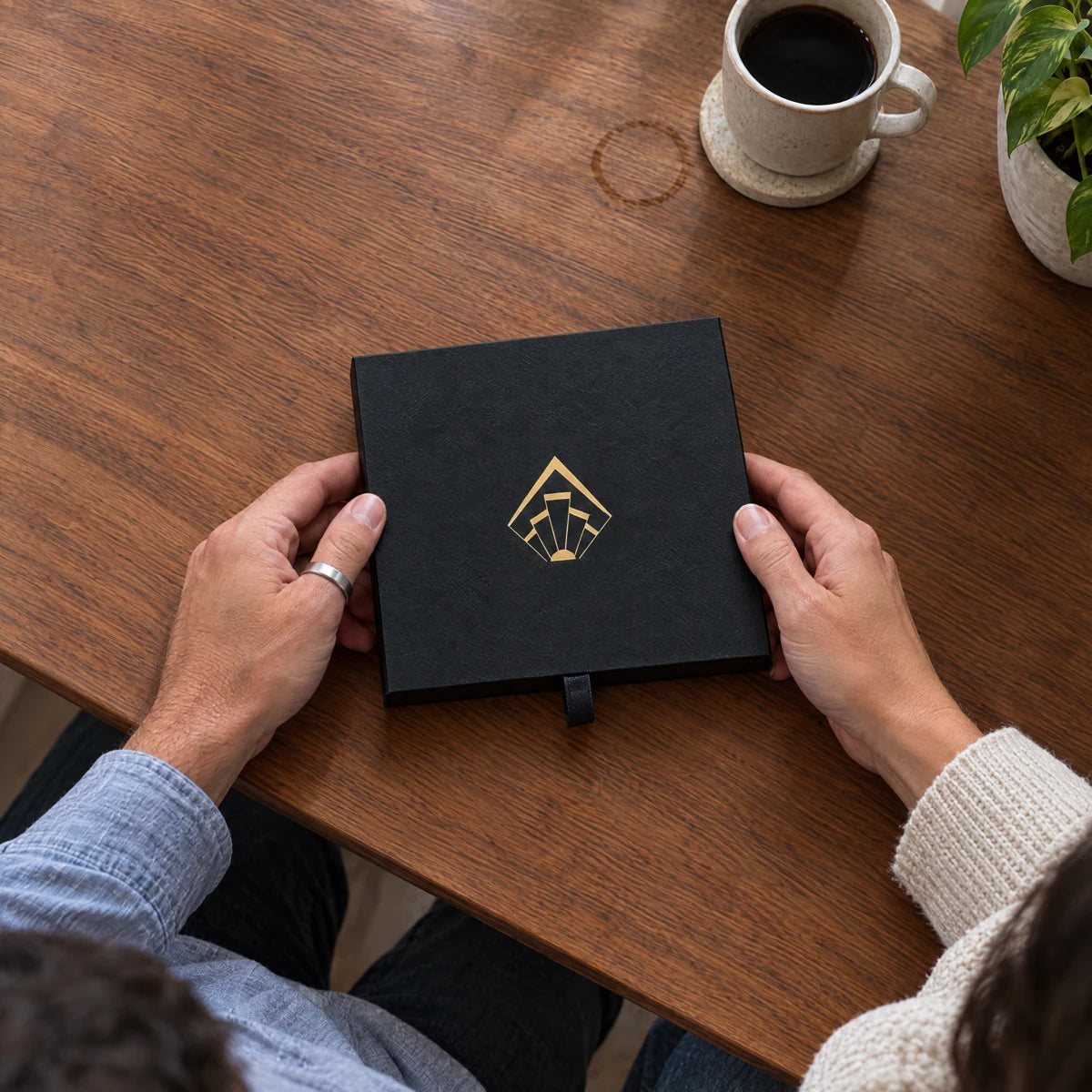 Two people holding the closed Twosome Poster carry box on a wooden table.