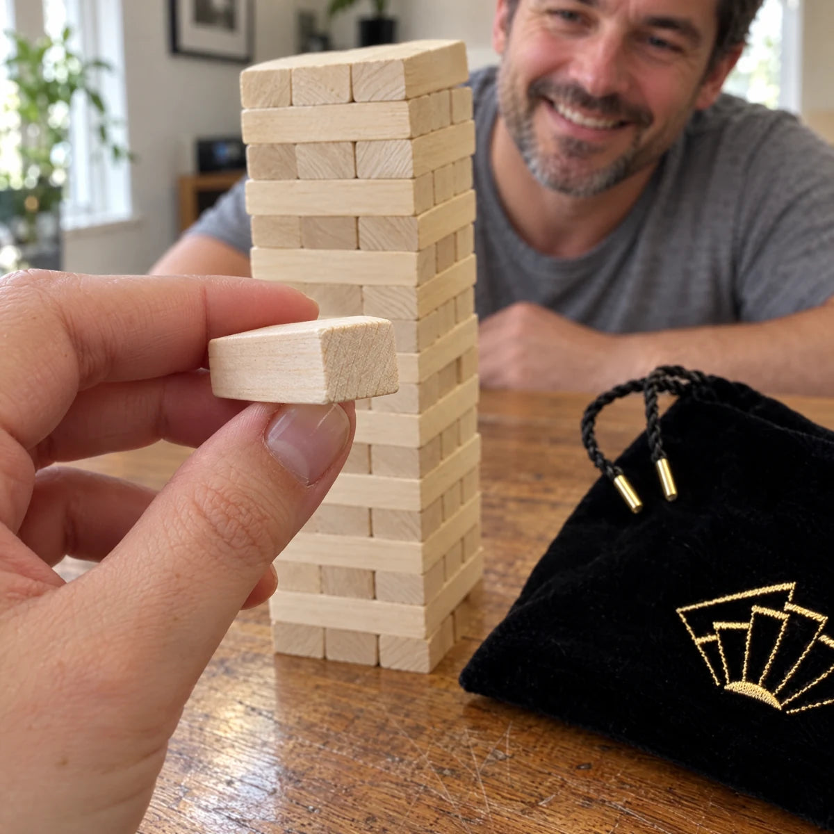 Close view of a hand holding a wooden block beside the Tease Tower and pouch.